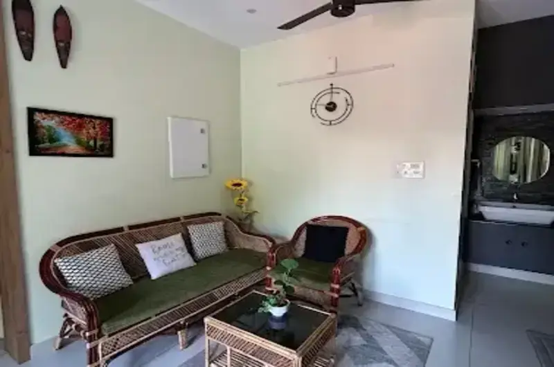 Cozy indoor living room and guest seating lounge inside The Nest Homestay Kovalam featuring wooden sofas.