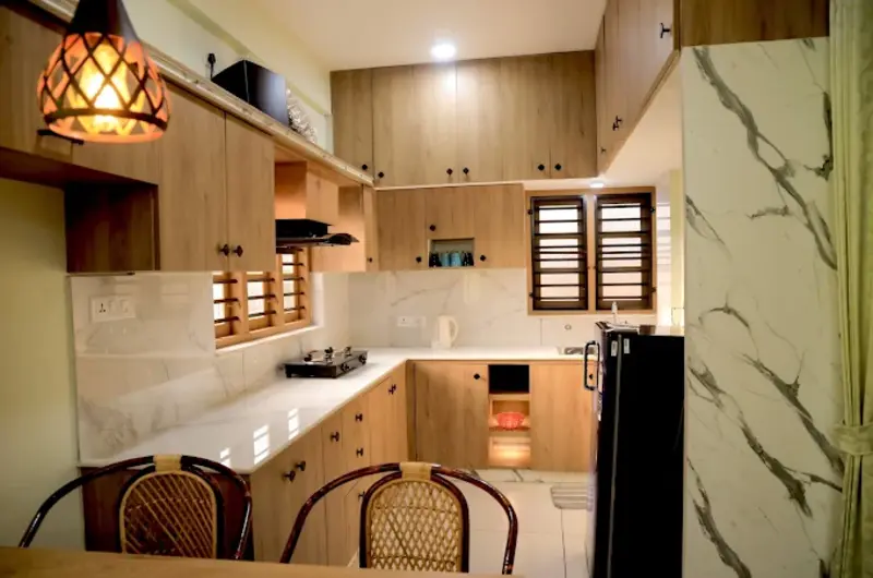 Modern kitchen setup with elegant wooden cabinetry and essential appliances at The Nest Homestay Kovalam.