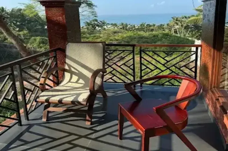 Private balcony lounge area featuring a wooden armchair and panoramic views at Jeevan Homestay Kovalam.