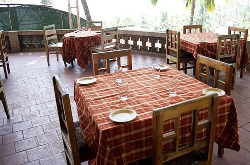 In house restaurant dining setup with wooden tables at Raja Hotel Kovalam