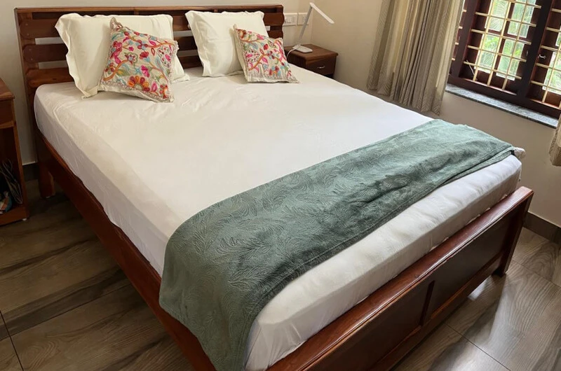 Cozy double bedroom setup with neat linens and a teal throw blanket at Laures House Kovalam