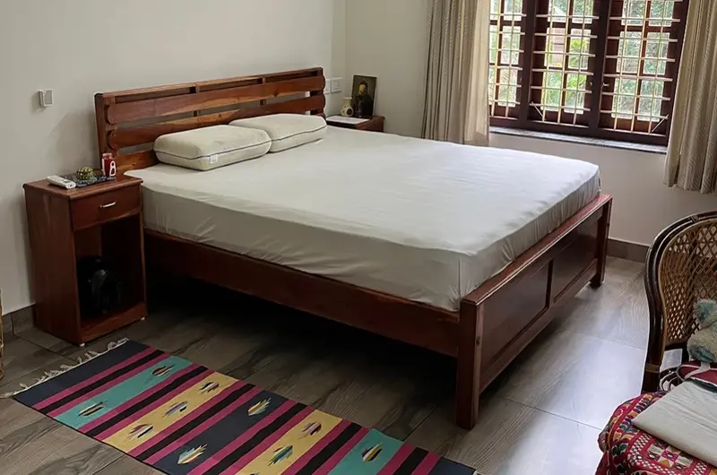Comfortable double bed with wooden frame and traditional floor rug at Laures House Kovalam