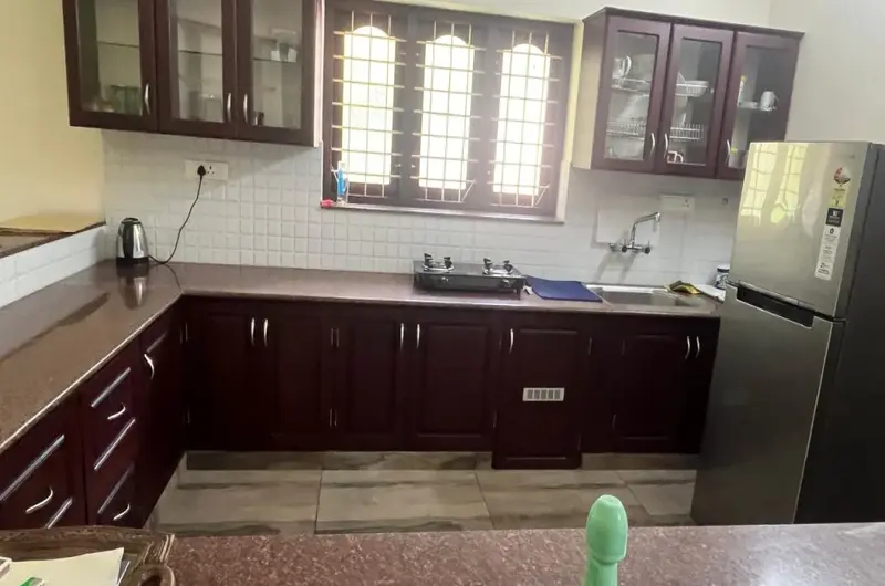 Modern self-catering kitchen with wooden cabinets and refrigerator at Laures House Kovalam