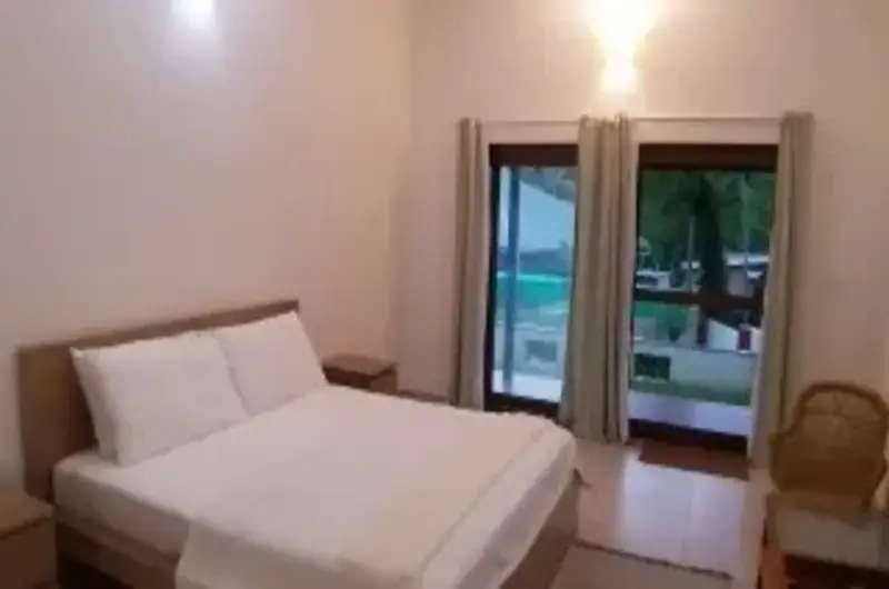 Minimalist boutique bedroom with premium bedding and glass balcony doors at The Ixora Kovalam.