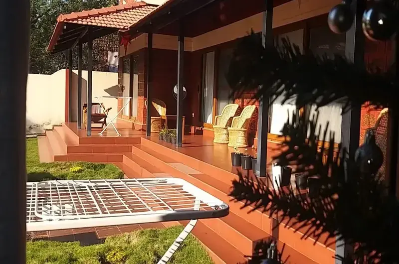 ModernWarmly lit traditional verandah sit-out with wooden pillars and brick flooring at The Ixora Homestay. rustic architecture showcasing red brick walls and large glass windows