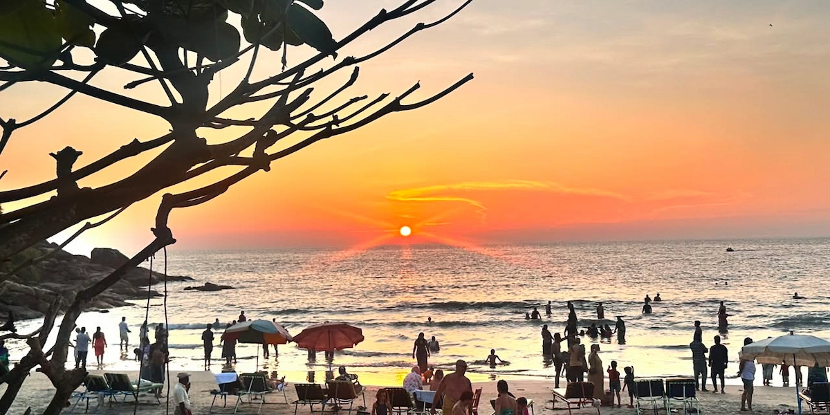 Sunset landscape over Kovalam beach coastline with tourists walking along the sandy shore in Kerala