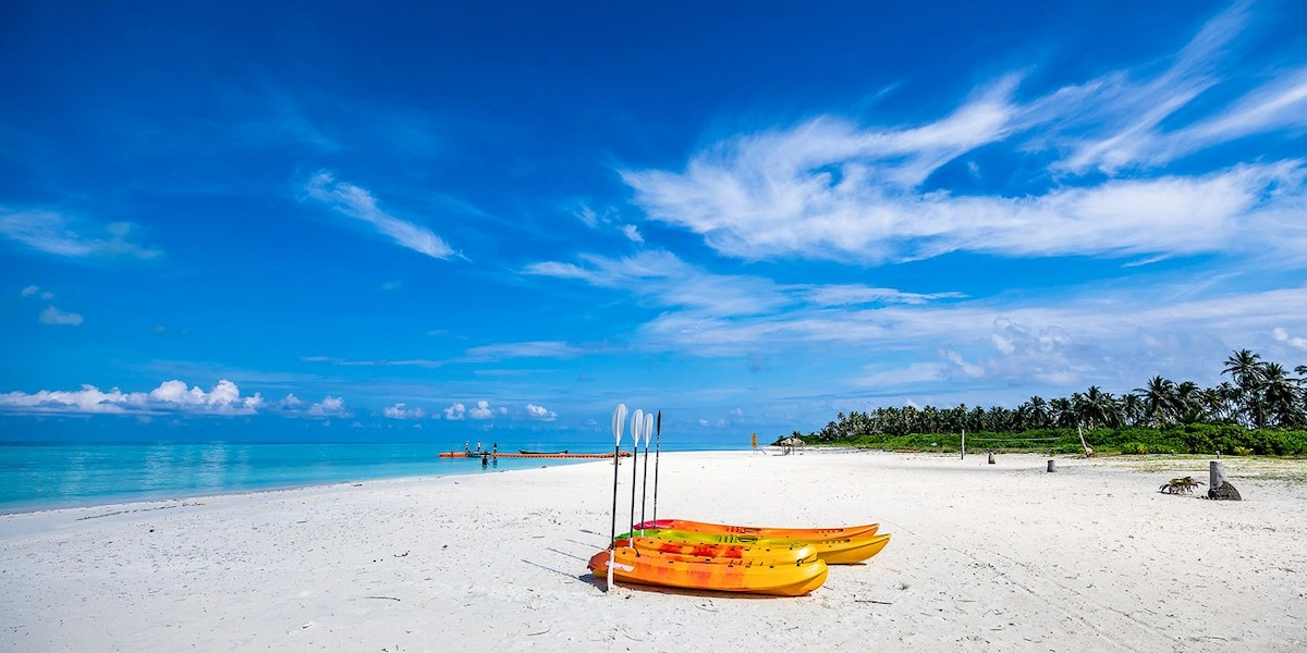 Yellow kayak rests on sandy tropical beach with clear blue sea and palm trees in Lakshadweep