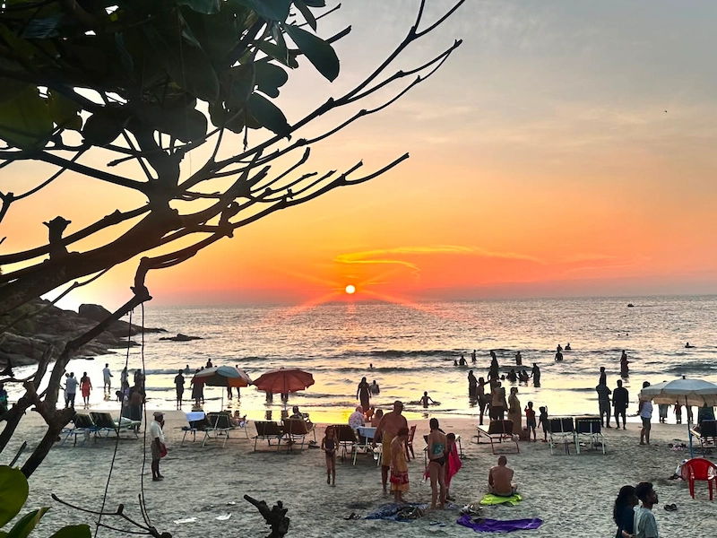 Scenic sunset view of Kovalam beach with palm tree silhouettes and visitors enjoying the shoreline