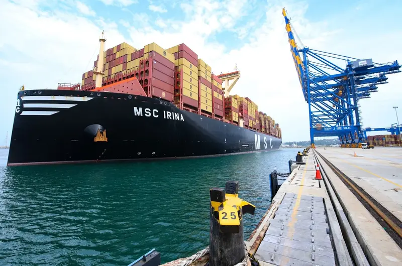 Massive cargo container ship docked at the wharf next to tall blue harbor cranes at Vizhinjam Port near Kovalam Kerala